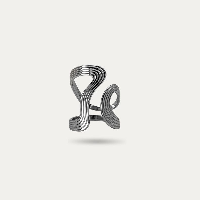 May include: A silver-colored ring with a unique, abstract design. The ring features multiple curved, wave-like bands that create an open, flowing shape. The metal has a polished finish, reflecting light and adding to its modern aesthetic.
