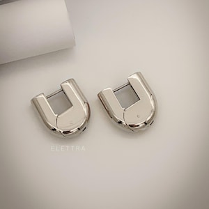 May include: A pair of silver hoop earrings with a unique U-shaped design. The earrings are made of metal and have a polished finish.