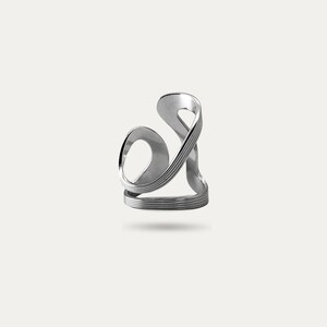 May include: A silver-colored ring with an abstract design. The ring features a looping, flowing shape with multiple bands and curves. The design is modern and sculptural, with a polished finish. The ring appears to be made of metal.