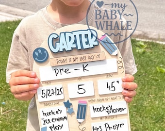 May include: A young child holds a wooden sign with the name "CARTER" and details about their last day of Pre-K. The sign includes the date, age 5, and height 45 inches. The child is wearing a beige shirt and black shorts.