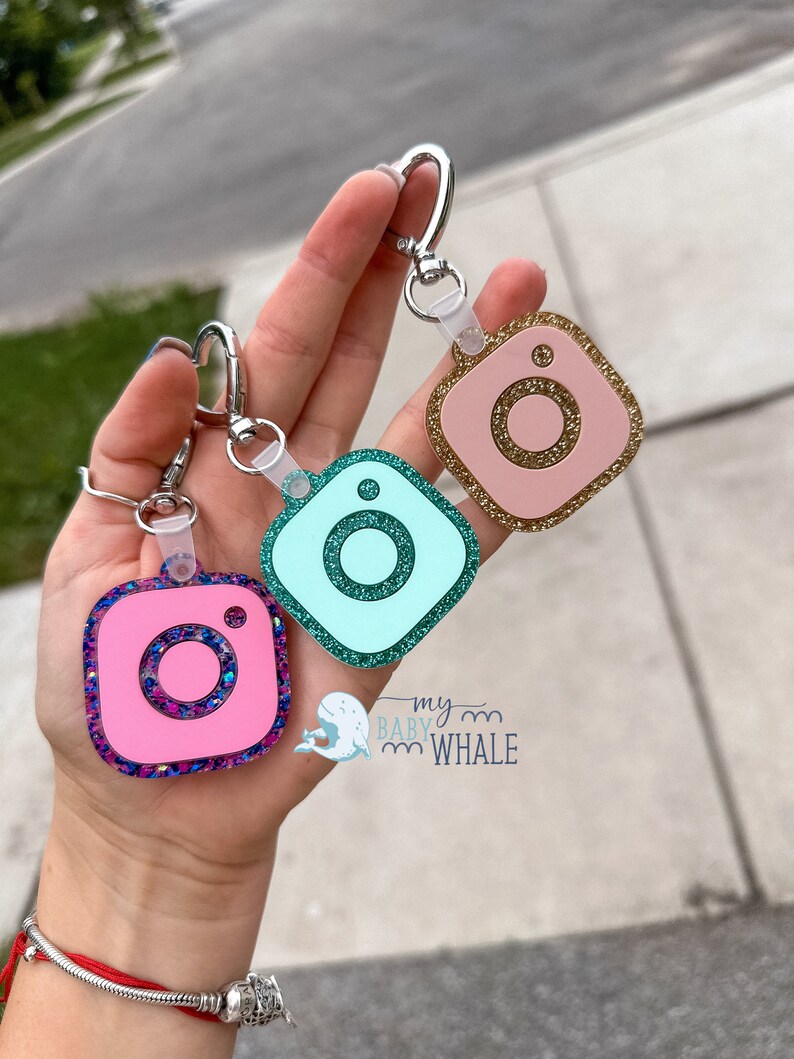 May include: Three Instagram-themed keychains with glitter accents. The keychains are pink, teal, and gold. Each keychain features a silver ring and a clear plastic loop.