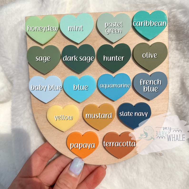 May include: A wooden board with 16 heart-shaped paint chips in various colors, including honeydew, mint, pastel green, caribbean, sage, dark sage, hunter, olive, baby blue, blue, aquamarine, french blue, yellow, mustard, slate navy, papaya, and terracotta. The board has the text "my baby whale" at the bottom.