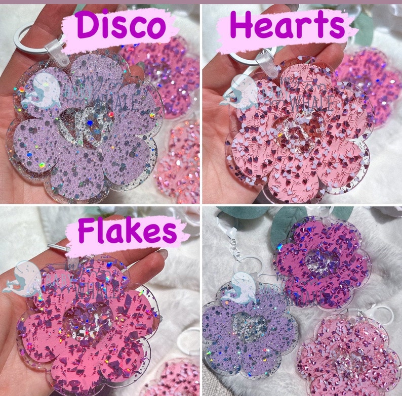K&ouml;nnte beinhalten: Vier bl&uuml;tenf&ouml;rmige Schl&uuml;sselanh&auml;nger mit Glitzer und Herz- oder Flockenakzenten. Die Schl&uuml;sselanh&auml;nger sind in Rosa- und Lilat&ouml;nen gehalten. Der Text "Disco", "Hearts" und "Flakes" ist auf dem Bild zu sehen. Jeder Schl&uuml;sselanh&auml;nger hat einen silberfarbenen Ring.