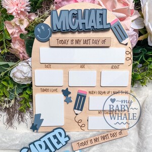 May include: Wooden school memory board with the name "MICHAEL" in blue letters. Includes spaces for date, age, height, and "Things I Love." Features a pencil and star accents, and the text "Today is my last day of" and "Today is my first day of."
