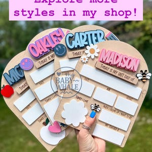 May include: Wooden milestone boards with names like Oakley, Carter, and Madison. Each board has spaces for dates, things loved, age, and weight, with decorative elements such as a bee, flower, and smiley face. The boards are heart-shaped.