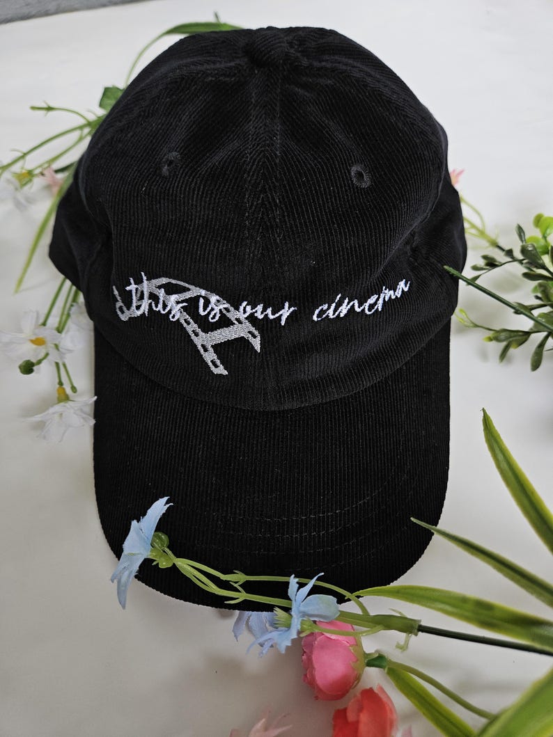 Puede incluir: Gorra de b&eacute;isbol de pana negra con bordado blanco que dice "This is our cinema" y un gr&aacute;fico de carrete de pel&iacute;cula.