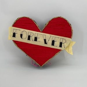May include: A red heart-shaped pinata with a yellow banner that says "FOREVER" in black lettering.