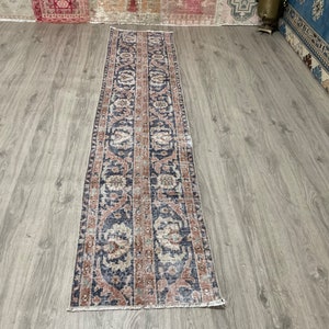 May include: A long, narrow rug with a blue, pink, and cream floral pattern. The rug has a distressed, vintage look.