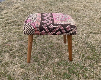 May include: A small, square ottoman with a brown and pink patterned fabric top and wooden legs.