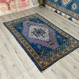May include: A vintage rug with a purple, blue, and yellow geometric pattern. The rug has a fringed edge and is made of wool.