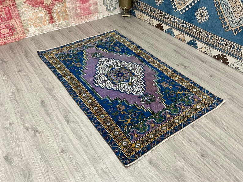 May include: A vintage rug with a purple, blue, and yellow geometric pattern. The rug has a fringed edge and is made of wool.
