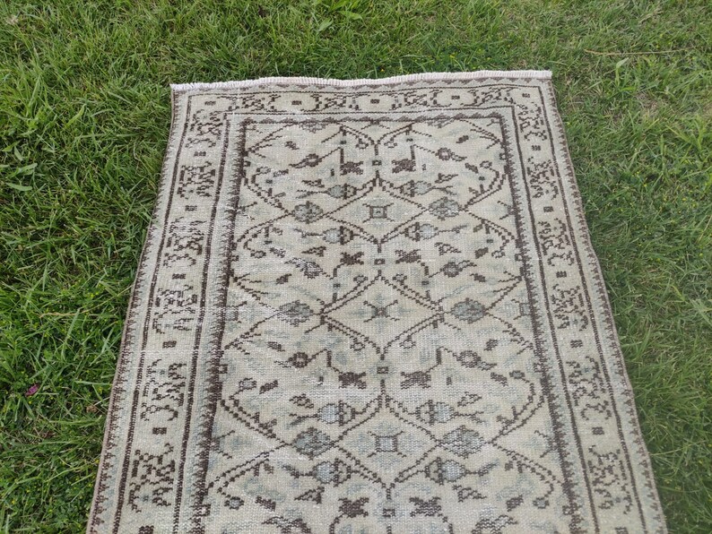 Peut inclure: Un tapis de couloir vintage avec un fond cr&egrave;me et un motif g&eacute;om&eacute;trique brun. Le tapis a une bordure &agrave; franges.