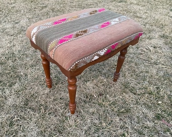 May include: A small wooden stool with a woven fabric seat featuring a geometric pattern in shades of brown, pink, and white. The stool has turned legs.