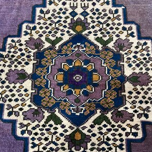 May include: A vintage rug with a purple background and a central medallion featuring a floral design in shades of blue, yellow, and green.