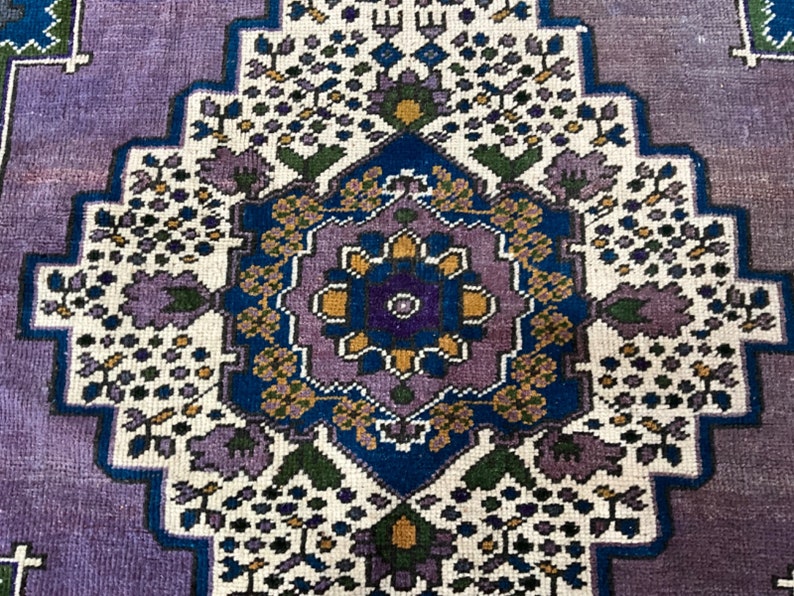 May include: A vintage rug with a purple background and a central medallion featuring a floral design in shades of blue, yellow, and green.