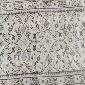 Peut inclure: Un tapis vintage avec un fond beige clair et un motif r&eacute;p&eacute;t&eacute; de motifs floraux brun fonc&eacute; et bleu clair. Le tapis a une bordure brune avec un motif r&eacute;p&eacute;t&eacute; de petits carr&eacute;s.