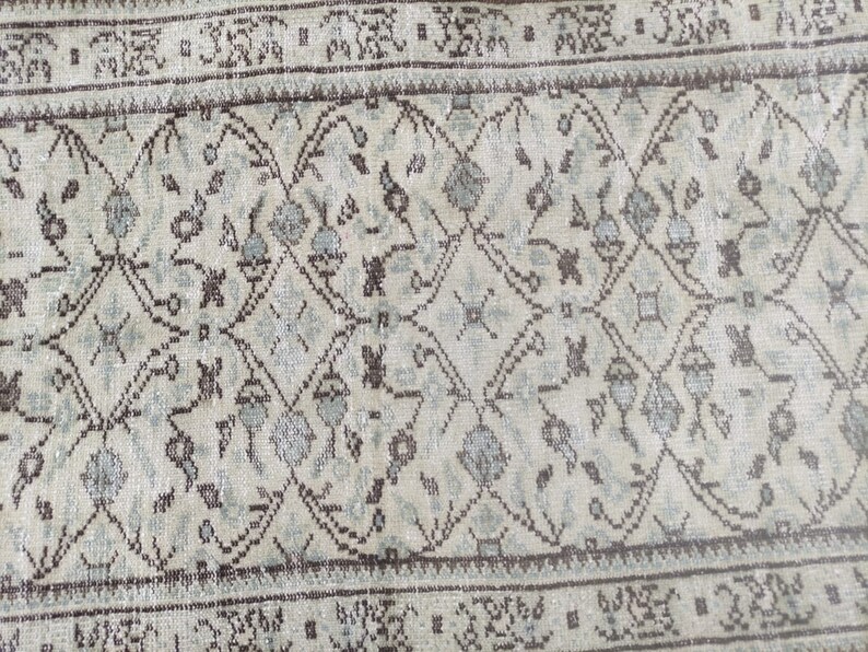 Peut inclure: Un tapis vintage avec un fond beige clair et un motif r&eacute;p&eacute;t&eacute; de motifs floraux brun fonc&eacute; et bleu clair. Le tapis a une bordure brune avec un motif r&eacute;p&eacute;t&eacute; de petits carr&eacute;s.