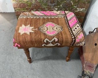 May include: A brown wooden stool with a pink and white patterned cushion. The cushion has a geometric design with a star in the center.