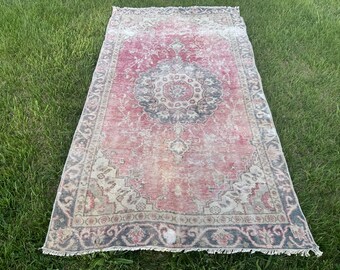 May include: A vintage pink and cream rug with a faded floral pattern and a dark gray border. The rug has a fringed edge.