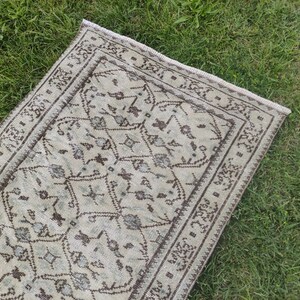 Peut inclure: Un tapis de couloir vintage avec un fond beige clair et un motif g&eacute;om&eacute;trique brun. Le tapis a une bordure frang&eacute;e.