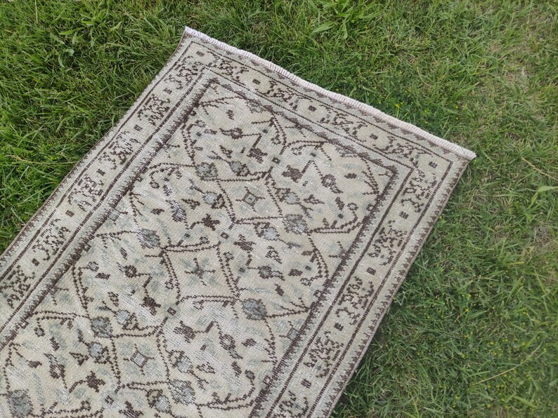 Peut inclure: Un tapis de couloir vintage avec un fond beige clair et un motif g&eacute;om&eacute;trique brun. Le tapis a une bordure frang&eacute;e.
