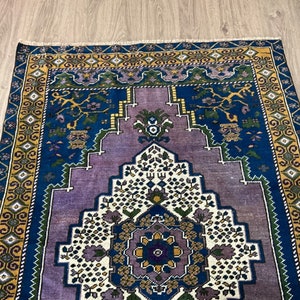 May include: A vintage rug with a blue, purple, and white geometric pattern. The rug has a gold and green border.