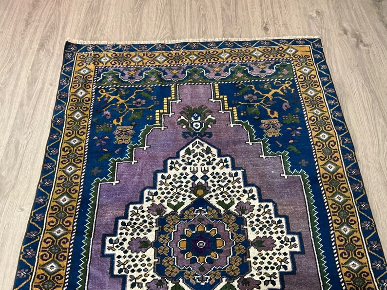 May include: A vintage rug with a blue, purple, and white geometric pattern. The rug has a gold and green border.