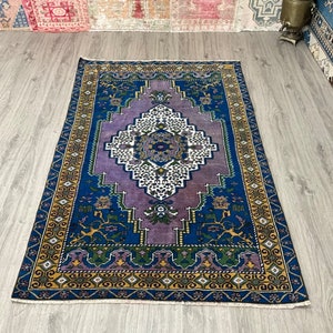 May include: A vintage rug with a purple, blue, and gold geometric pattern. The rug has a central medallion with a white and blue design.
