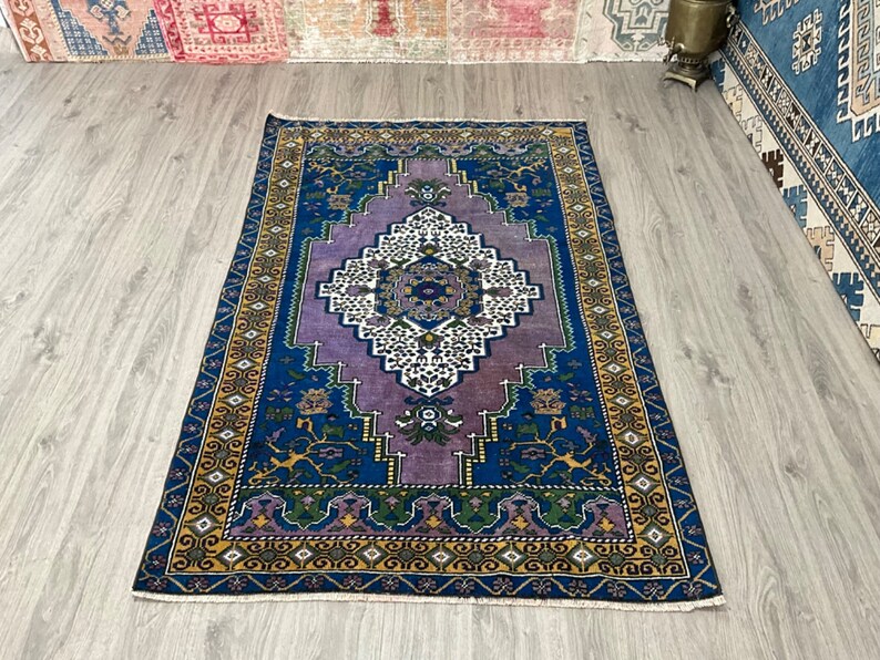 May include: A vintage rug with a purple, blue, and gold geometric pattern. The rug has a central medallion with a white and blue design.