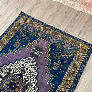 May include: A vintage rug with a purple, blue, and yellow geometric pattern. The rug has a fringed edge and is made of wool.