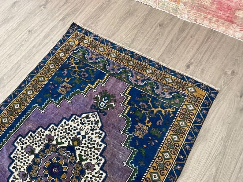 May include: A vintage rug with a purple, blue, and yellow geometric pattern. The rug has a fringed edge and is made of wool.