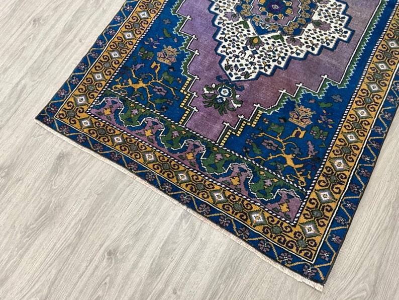 May include: A vintage rug with a purple, blue, and yellow geometric pattern. The rug has a fringed edge and is made of wool.