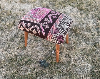 May include: A small, wooden stool with a colorful, patterned fabric seat. The fabric is a mix of pink, brown, and white, with geometric designs.