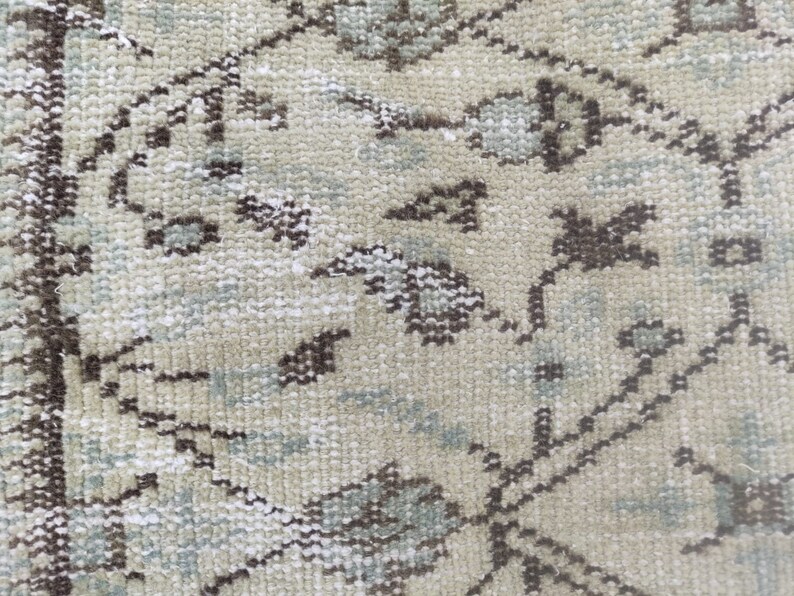 Peut inclure: Gros plan sur un tapis beige avec un motif floral dans les tons de brun et de bleu.