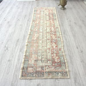 May include: A rectangular, vintage-style rug with a detailed pattern in shades of red, beige, and blue. The rug is placed on a light gray wooden floor, showcasing its intricate design and aged appearance. The rug's dimensions are not visible.