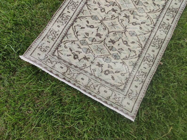 Peut inclure: Un tapis de couloir de style vintage avec un fond beige clair et un motif g&eacute;om&eacute;trique brun et bleu. Le tapis a une bordure frang&eacute;e.
