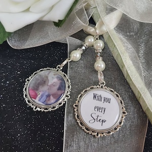May include: Two silver-toned charms with a white satin ribbon. One charm features a photo of a couple kissing, and the other charm has the text "With you every step".