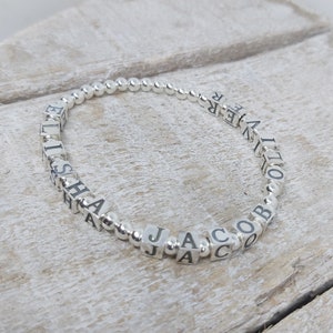 May include: Silver bead bracelet with the names "Elisha", "Jacob", and "Oliver" spelled out in silver letter beads.