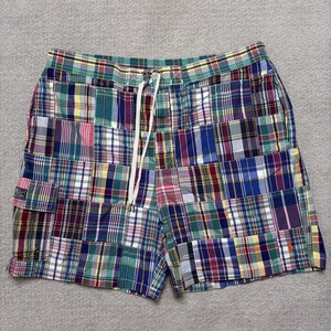 May include: Multi-colored plaid patchwork shorts featuring a drawstring waistband, a side cargo pocket with a flap, and a small embroidered logo on the lower right leg. The fabric consists of various intersecting squares of tartan patterns in blue, green, red, yellow, and white.