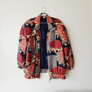May include: A red, blue, and cream patterned jacket with a zipper closure. The jacket has a patchwork design with floral and geometric patterns.