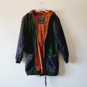 Può includere: Una giacca di pelle scamosciata blu, verde e marrone con cappuccio e chiusura con coulisse. La giacca ha un'etichetta che recita "ORIGINAL".