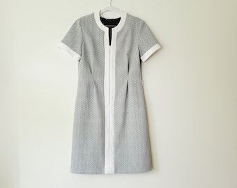 May include: A black and white short-sleeved dress with a white trim around the neckline and down the front. The dress has a simple, classic design.