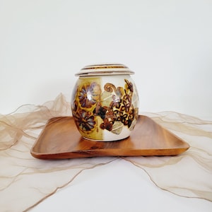 Könnte beinhalten: Eine weiße Keramikdose mit braunem Deckel und Blumenmuster. Die Dose steht auf einem Holztablett.
