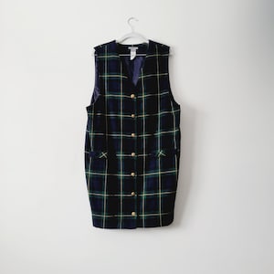 May include: A sleeveless plaid dress with a V-neckline and button closure. The dress has a green, yellow, and blue plaid pattern and features two pockets on the front.