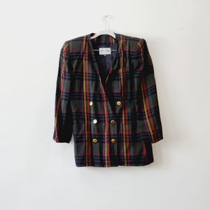 May include: A vintage plaid blazer in a mix of colors, including green, red, yellow, and purple. The double-breasted jacket features gold-colored buttons and is displayed on a white hanger against a white background.