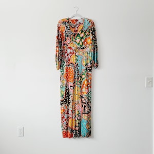 May include: A long, colorful maxi dress with a paisley print in shades of orange, blue, green, and black. The dress has a V-neckline and long sleeves.