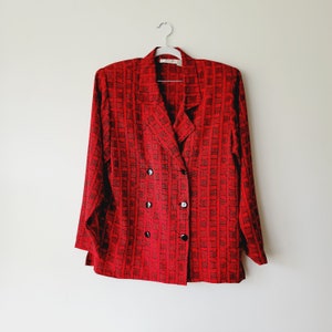 May include: A red blazer with a black and white geometric pattern. The blazer has a double-breasted closure with four black buttons.