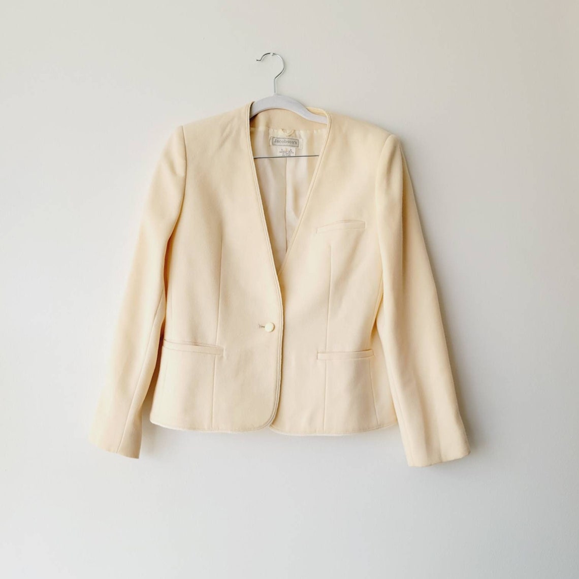 Tailored women's blazer in cream wool hanging on a wooden hanger
