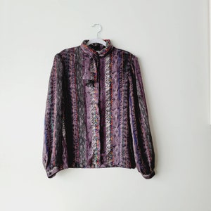 May include: A purple, long-sleeved blouse with a colorful geometric pattern and a bow tie at the neck.