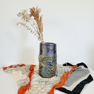 May include: A dark blue and green ceramic vase with a textured surface. The vase is filled with dried flowers and branches.
